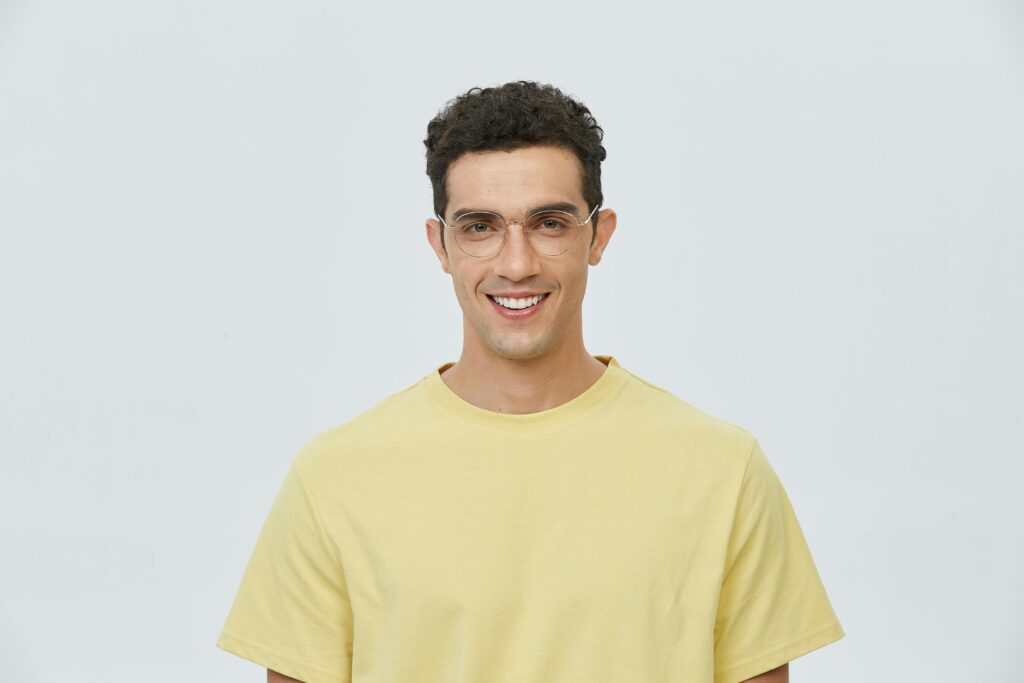 Portrait of a young man wearing glasses and a yellow shirt, smiling brightly.